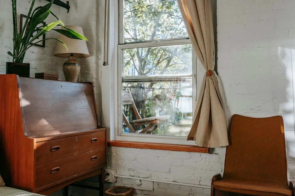 Sunlit reading corner with a plant, a soft chair, and a window overlooking greenery