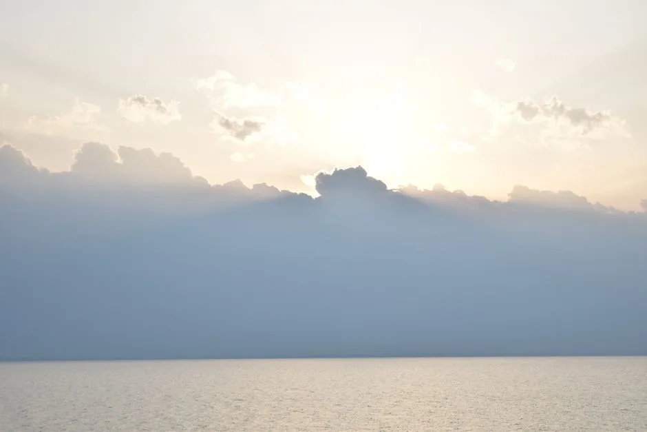 A soft sunrise over calm water, gentle light through clouds